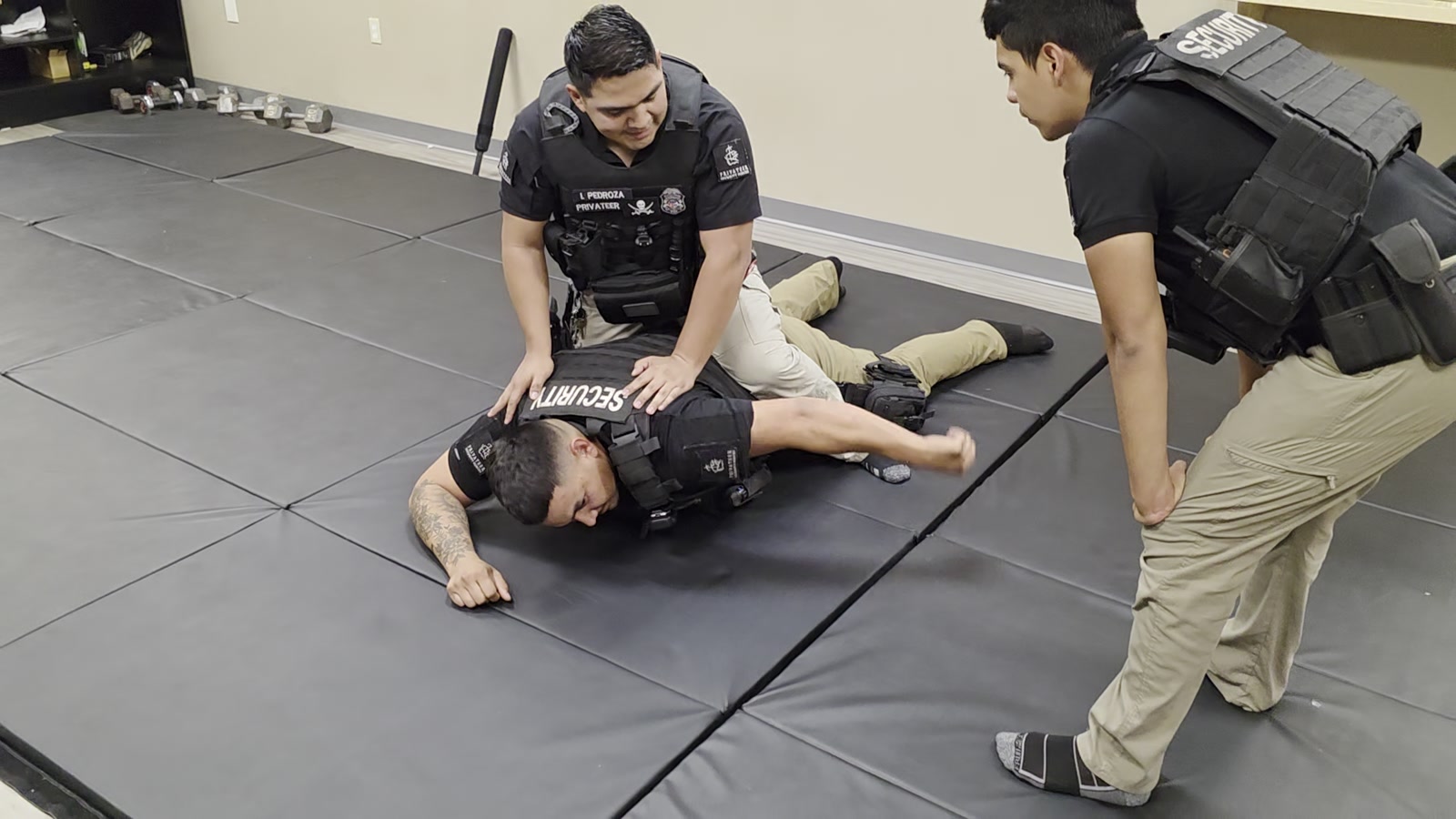 Privateer personnel practicing a supervised defensive-tactics control drill on training mats